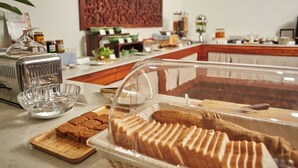 Zona de bufé con diversas opciones de comida, incluyendo pan y pastel, expuestos en un recipiente de plástico transparente.