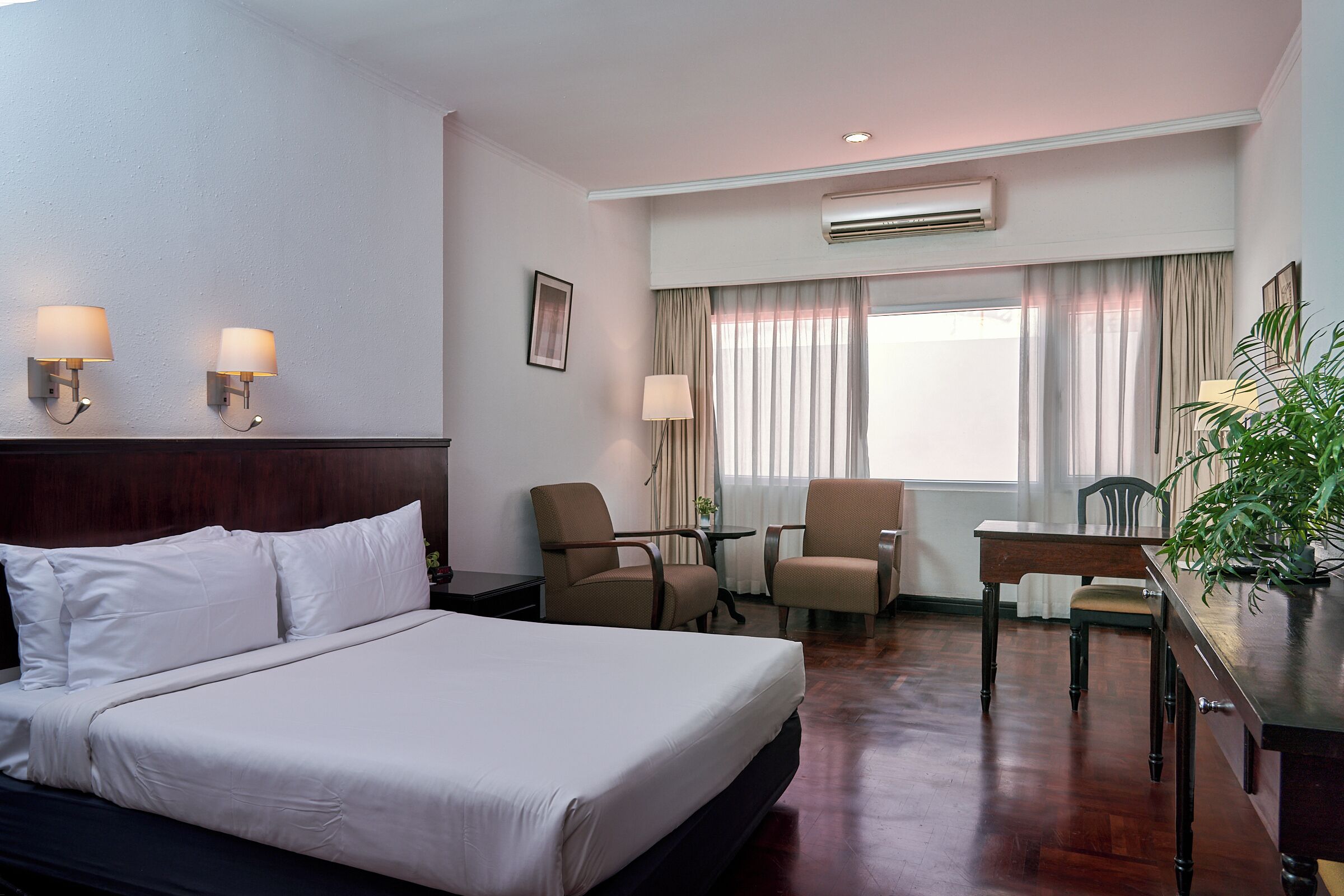A hotel room with a bed, two chairs, a desk, and a window with curtains.