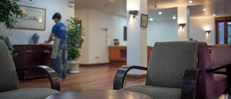 A hotel lobby with seating areas, a reception desk, and a person working at the desk.