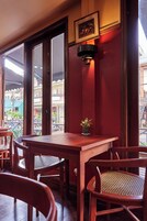 A wooden table with chairs, a small potted plant, and a wall-mounted light fixture in a room with large windows and a red wall.