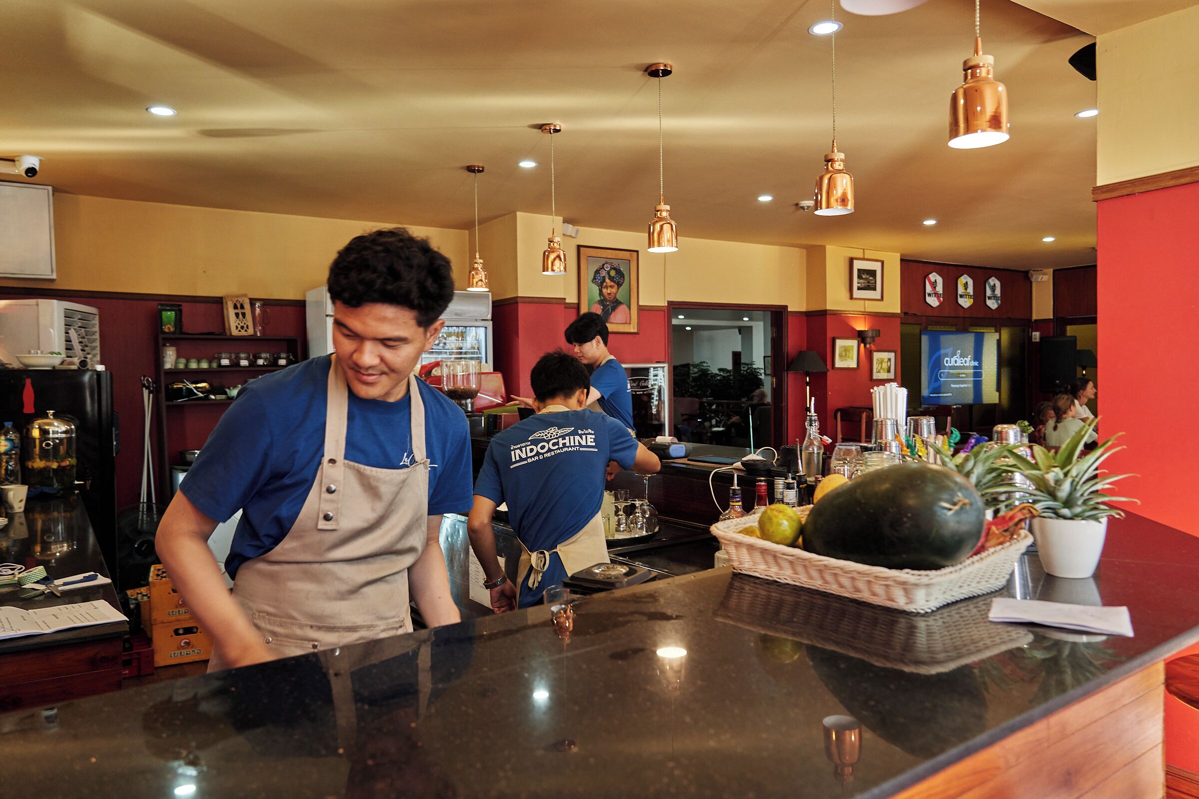 A bar area with a counter, hanging lights, and a potted plant.