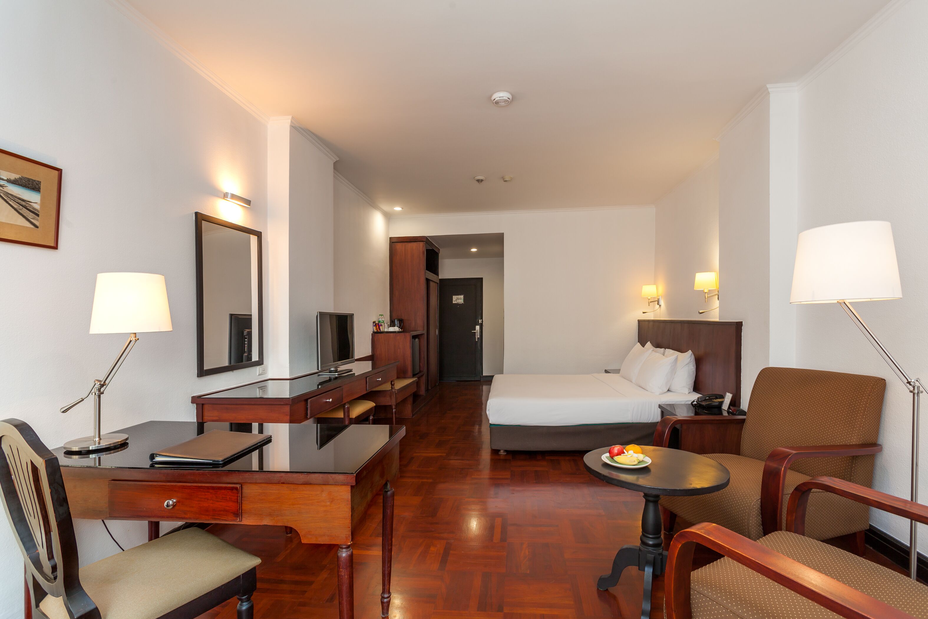 A hotel room with a bed, desk, chair, and a dining table with a plate of fruit.
