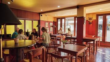 Un restaurant avec des tables et des chaises en bois, un coin bar et de grandes fenêtres laissant entrer la lumière naturelle.