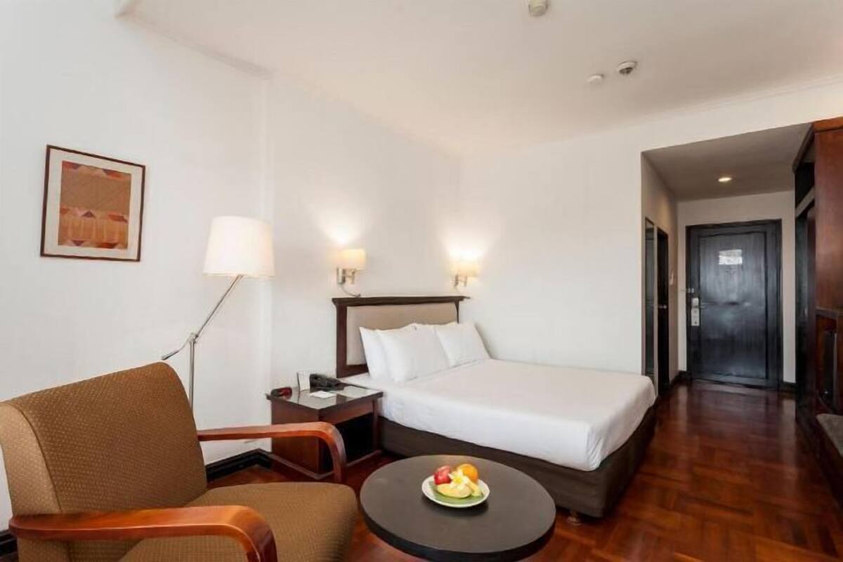 Een hotelkamer met een bed, een stoel, een bureau, een lamp en een schaal fruit.