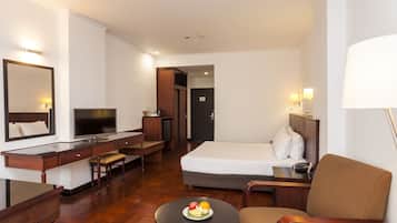 Habitación de hotel con cama, escritorio con silla, una pequeña mesa con fruta y televisión.