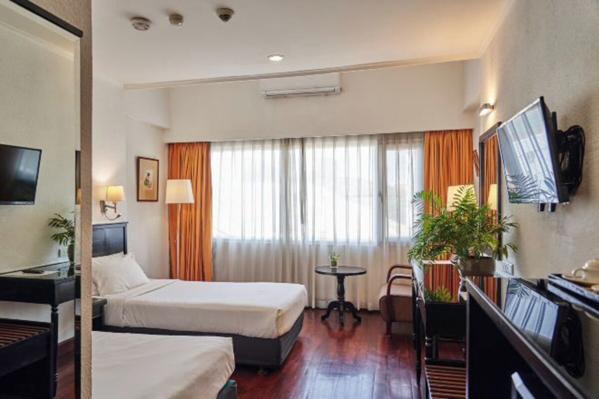 Habitación de hotel con dos camas, un escritorio, una silla, un televisor y una mesita con una planta.