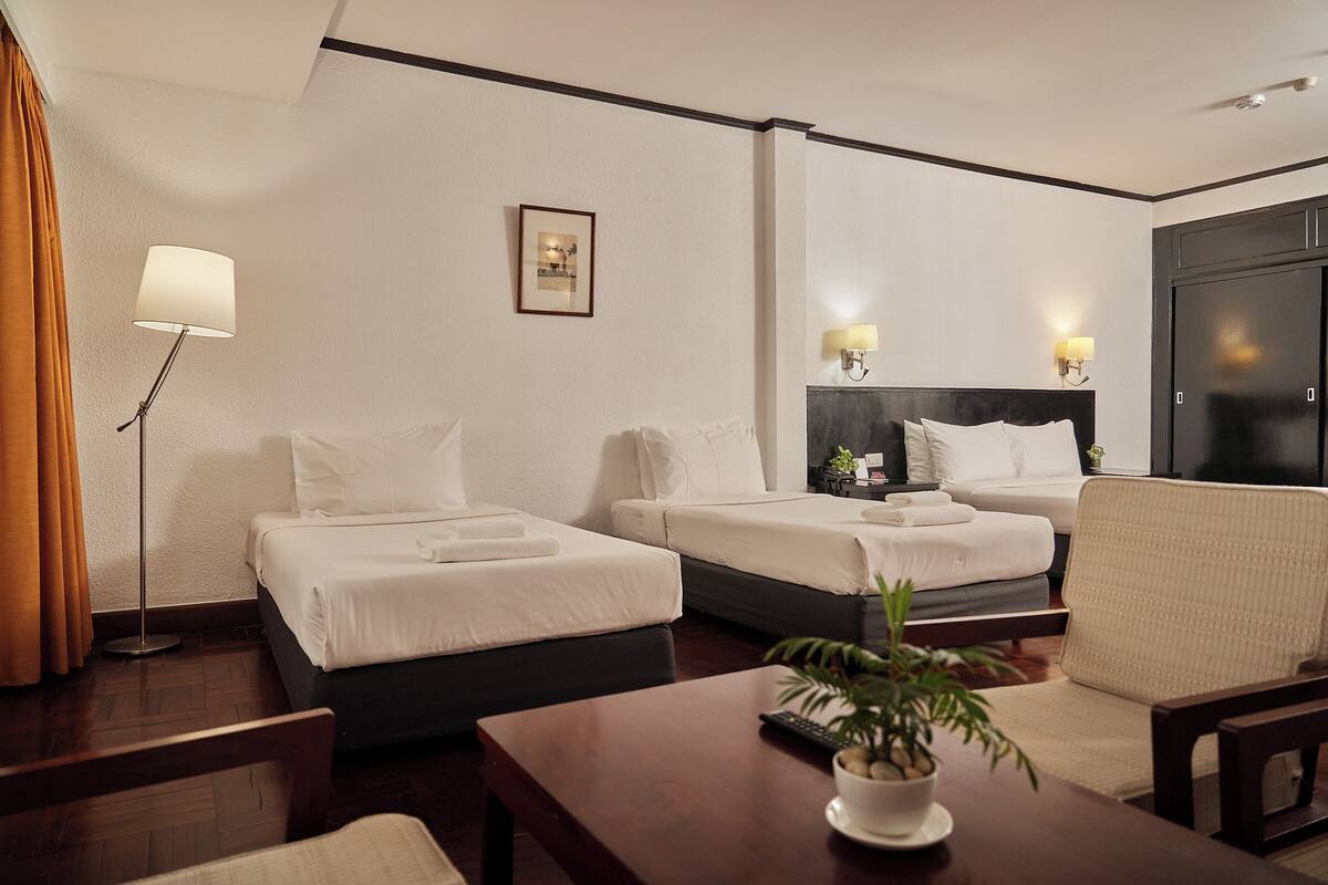 Een hotelkamer met twee bedden, een bureau, een stoel, een lamp en een ingelijste foto aan de muur.