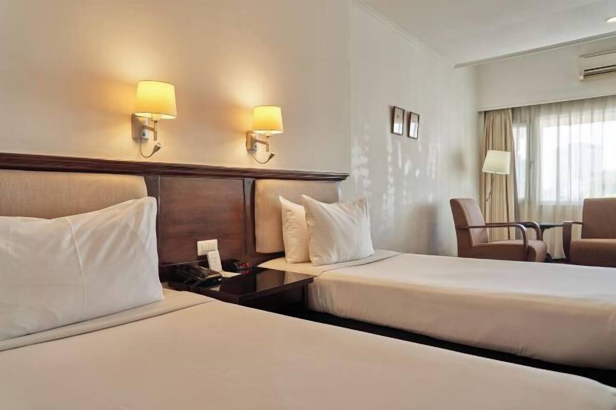 Ein Hotelzimmer mit zwei Betten, einem Schreibtisch, einem Stuhl und zwei Wandlampen.