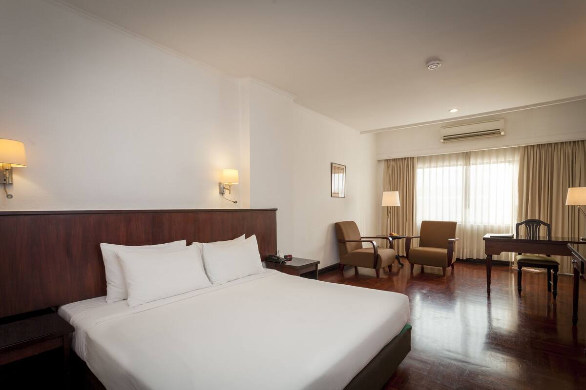 Een hotelkamer met een groot bed, twee stoelen, een bureau en een lamp.