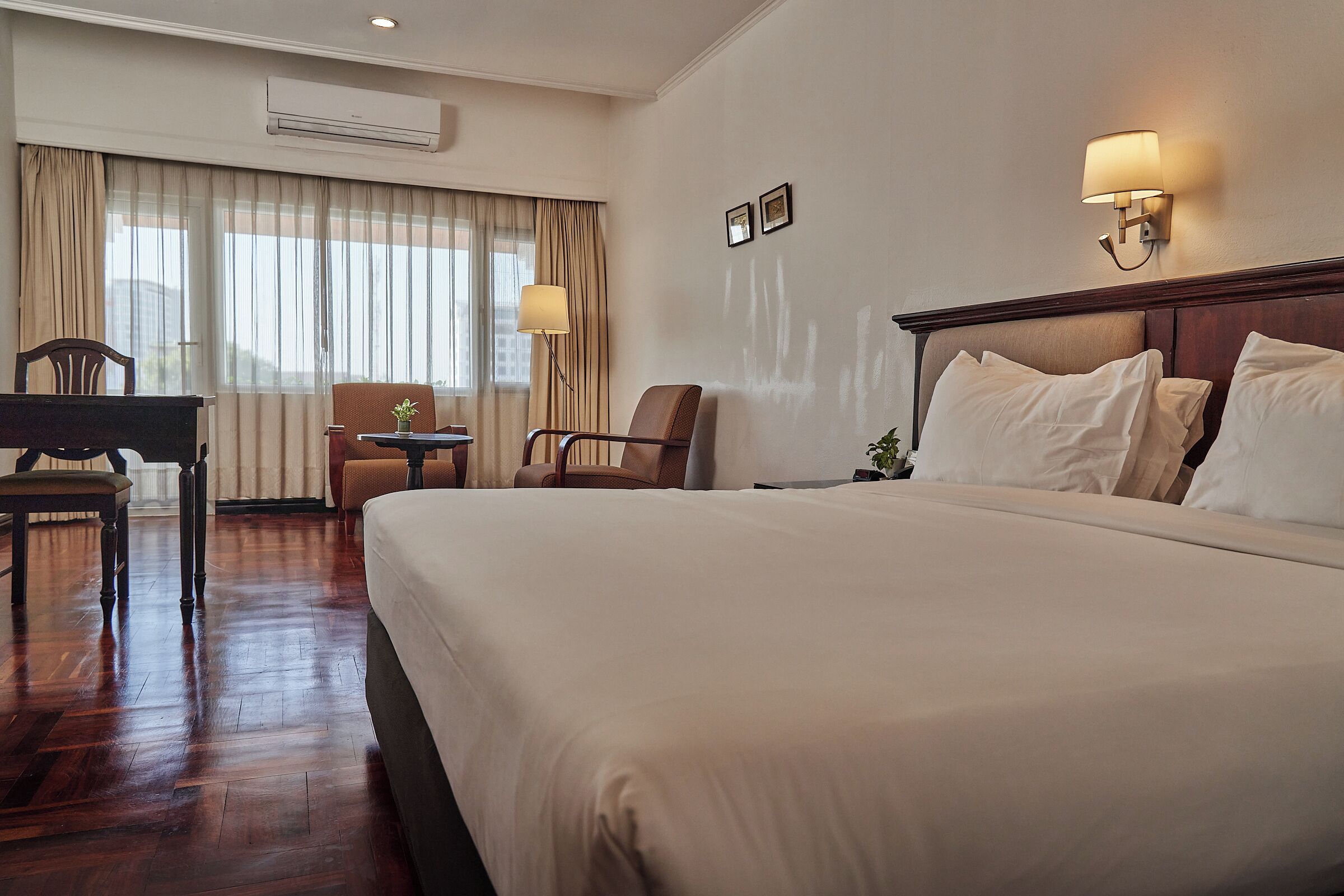 Ein Hotelzimmer mit einem großen Bett, einem Schreibtisch, zwei Stühlen, einer Lampe und einer Klimaanlage.
