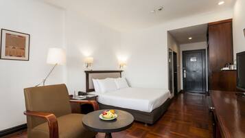 A hotel room with a bed, a chair, a small table with fruit, a lamp, and a television.