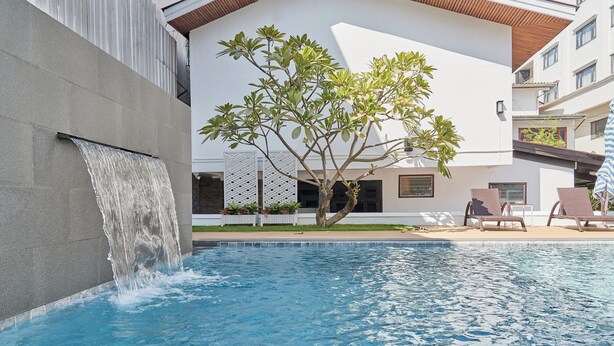 Una piscina con cascada, rodeada de sillas de descanso y un árbol.