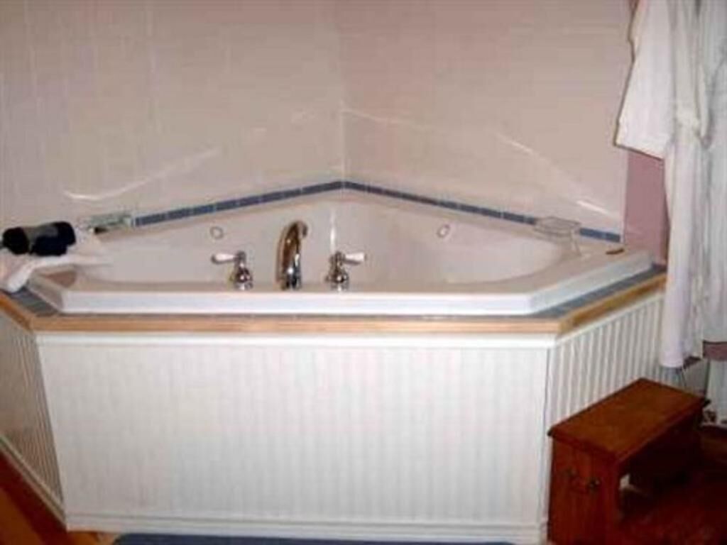 A corner bathtub with a wooden frame, a small wooden stool, and a towel hanging on the wall.