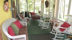 A covered porch with wicker furniture, a rocking chair, and a table. - Brookview Manor Inn (Canadensis)