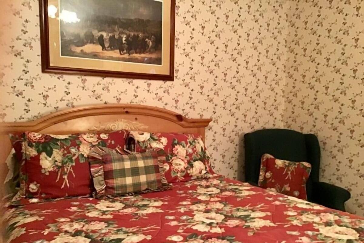 Ein Schlafzimmer mit einem floralen Bettbezug, einem Holzkopfteil und einem gerahmten Bild an der Wand.