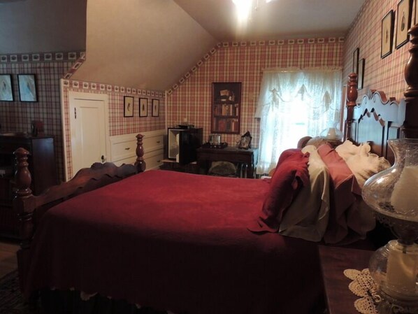 A bedroom with a large bed, a dresser, a desk, and a window with curtains.