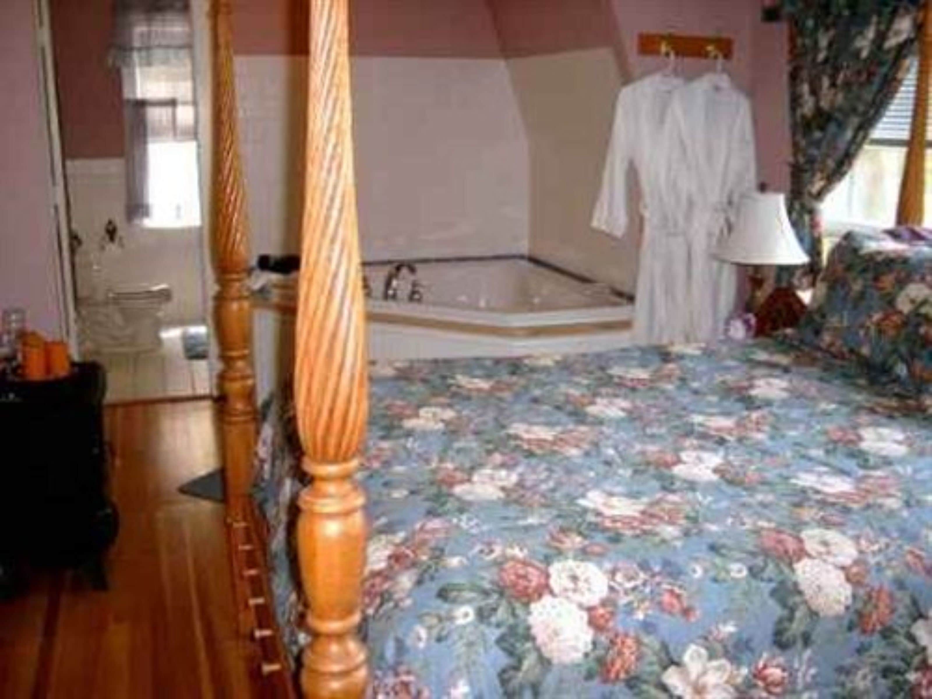 Un dormitorio con cama con dosel, un ventanal grande, una bañera y una colcha estampada con motivos florales.