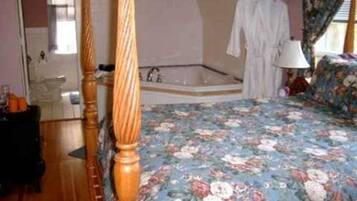 A bedroom with a four-poster bed, a large window, a bathtub, and a floral bedspread.