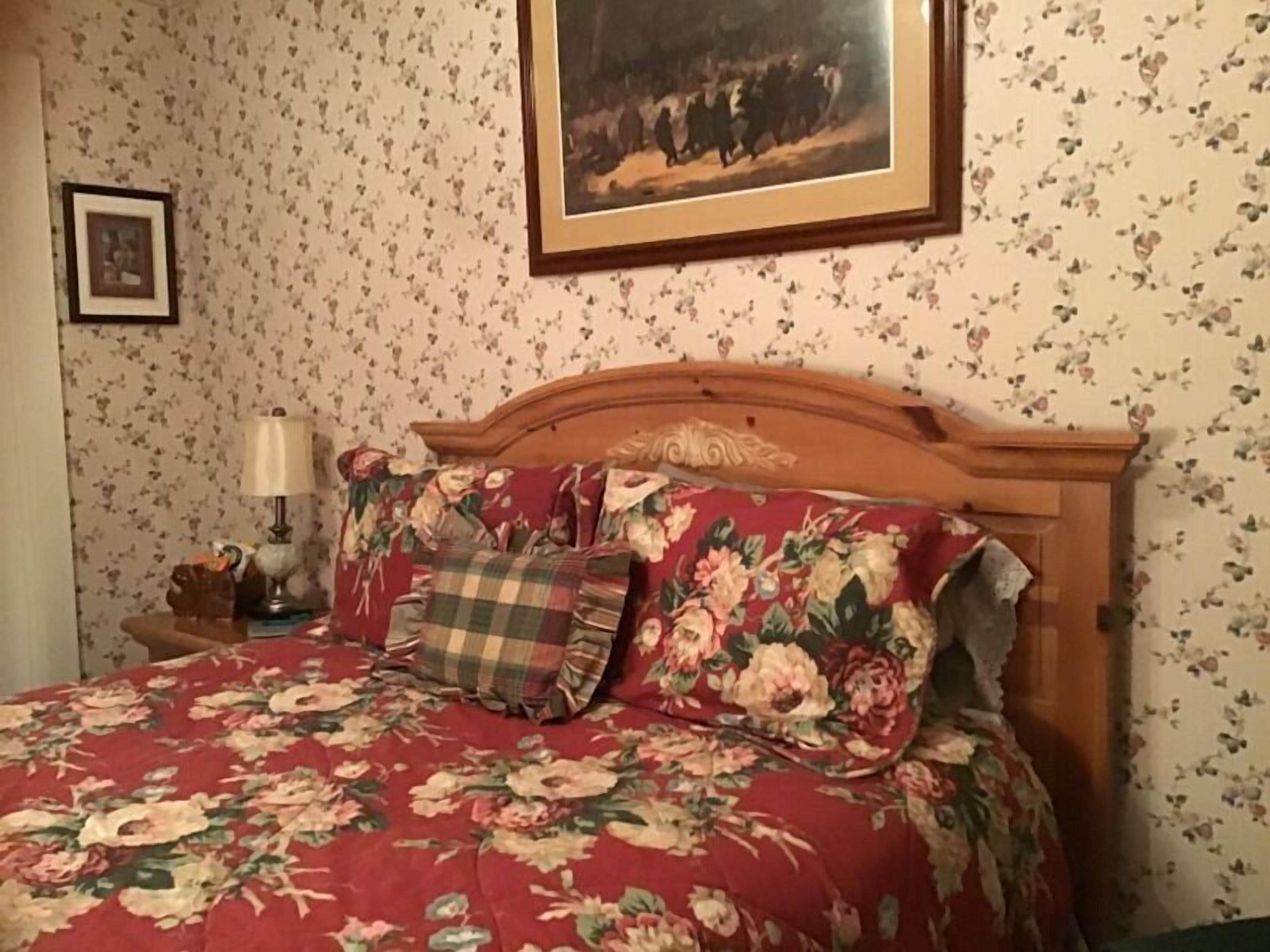 Um quarto com colcha estampada de flores, cabeceira de madeira e um quadro na parede.