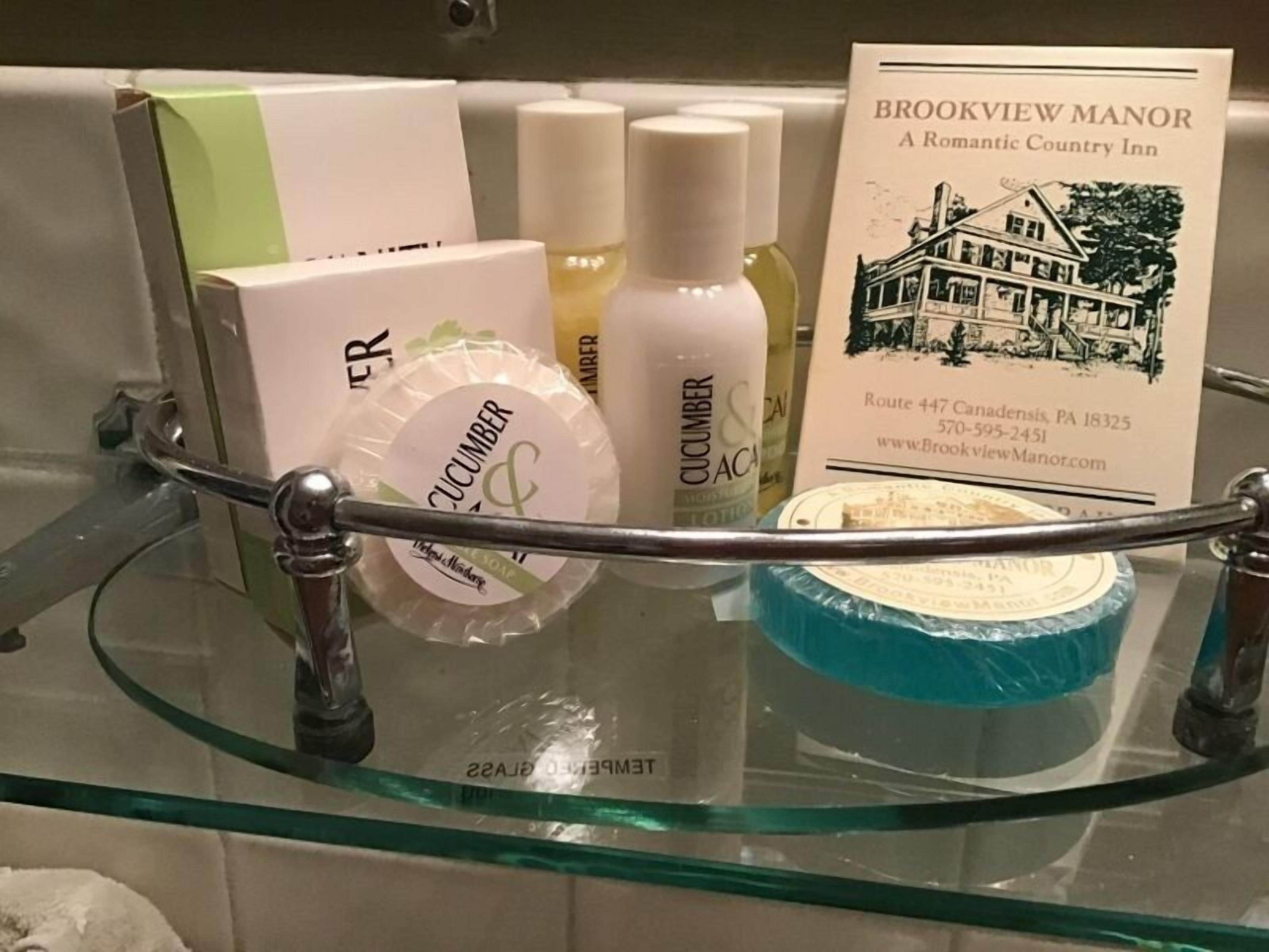 Uno scaffale in bagno con articoli da toilette, tra cui una saponetta all'aloe e al cetriolo, e un depliant per Brookview Manor.