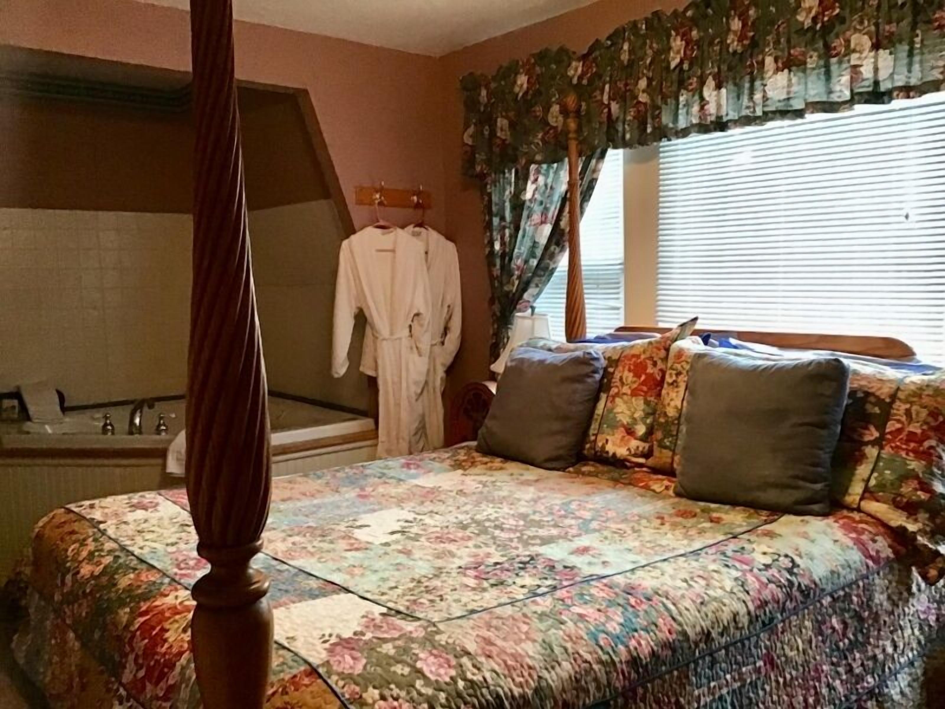Ein Schlafzimmer mit einem Himmelbett, einem großen Fenster mit Vorhängen, einer Badewanne und einem Bademantel, der an einem Haken hängt.