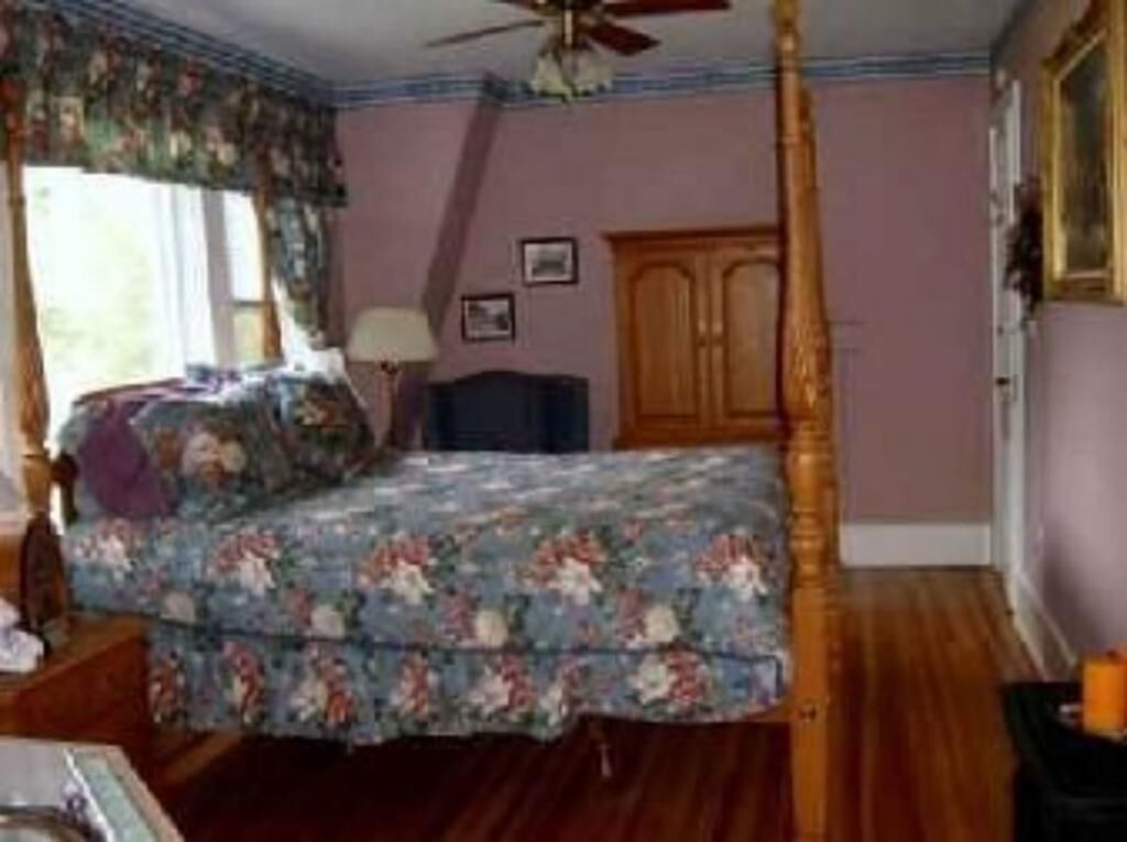 Ein Schlafzimmer mit Himmelbett, Holzboden und Deckenventilator.