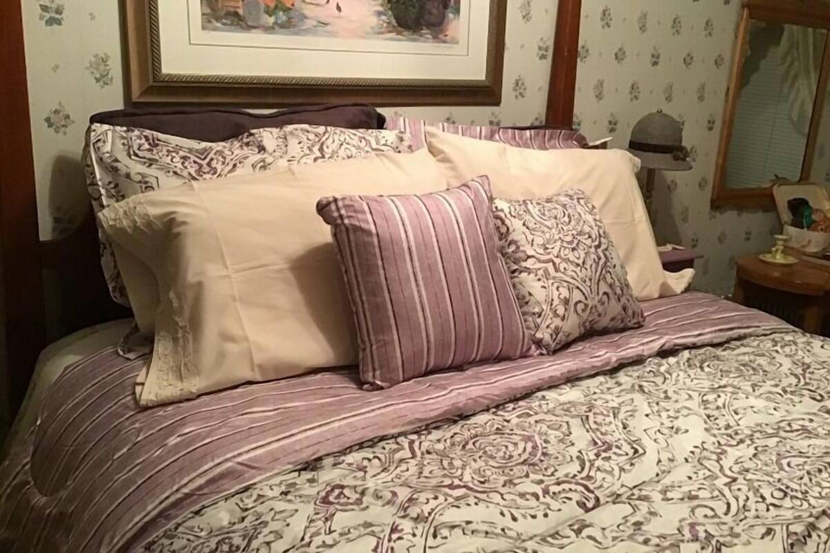 Ein Bett mit gemusterten Bettbezügen und mehreren Kissen, ein gerahmtes Gemälde darüber und ein Spiegel an der Wand.