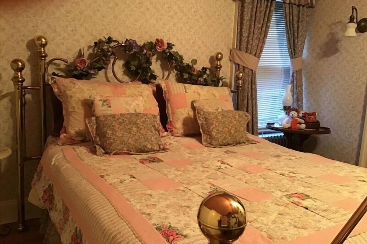Ein Schlafzimmer mit einem Bett, einer blumigen Tagesdecke und einem Nachttisch mit Teddybär und Tasche.