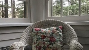 A wicker chair with floral upholstery near a window with a view of trees. - Brookview Manor Inn (Canadensis)