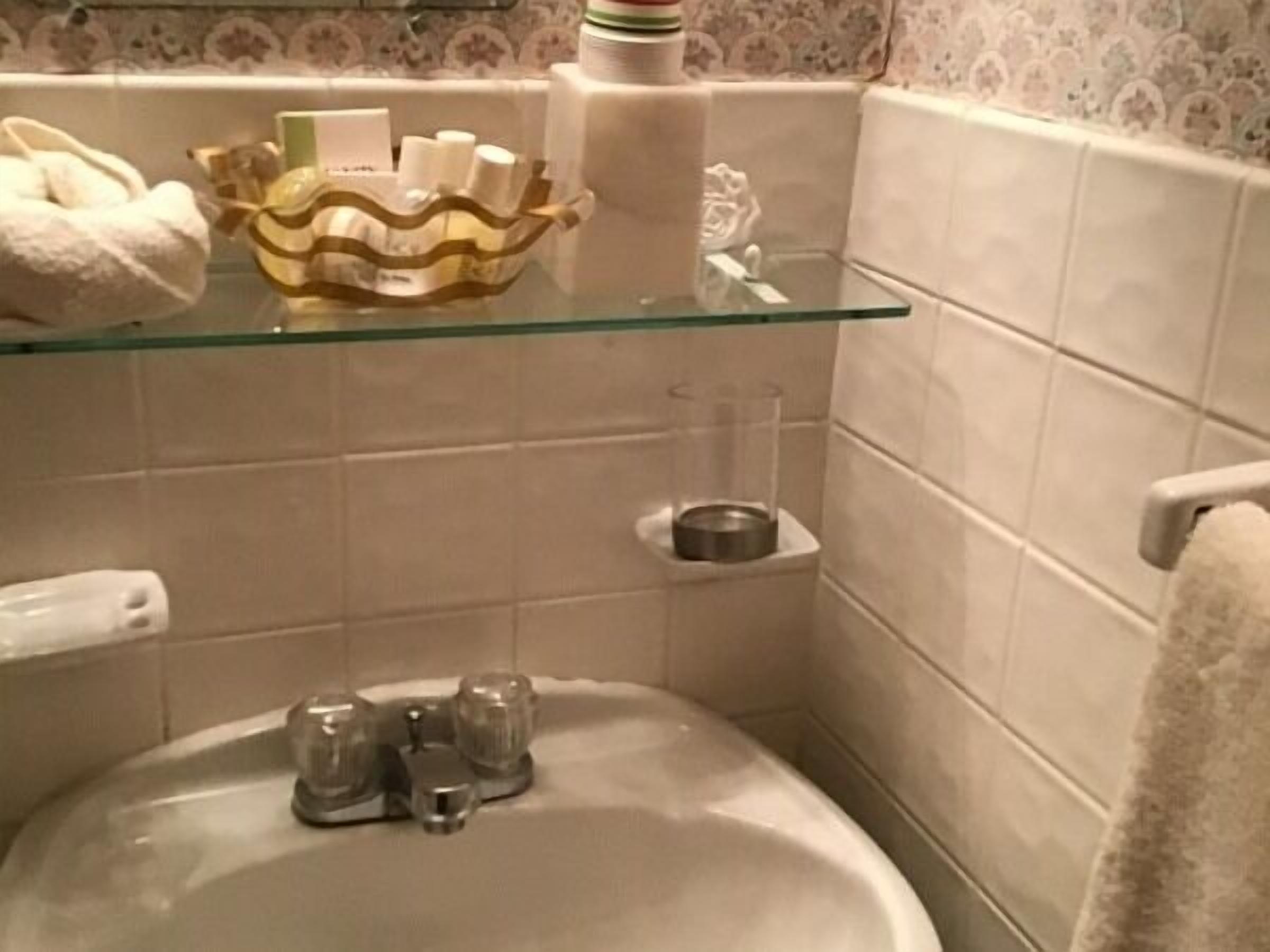 Une salle de bain avec une étagère en verre où sont rangés les articles de toilette, un lavabo avec un robinet et un porte-serviettes.