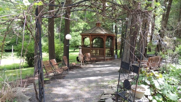 A gazebo with benches and a gravel path in a wooded area. - Brookview Manor Inn (Canadensis)