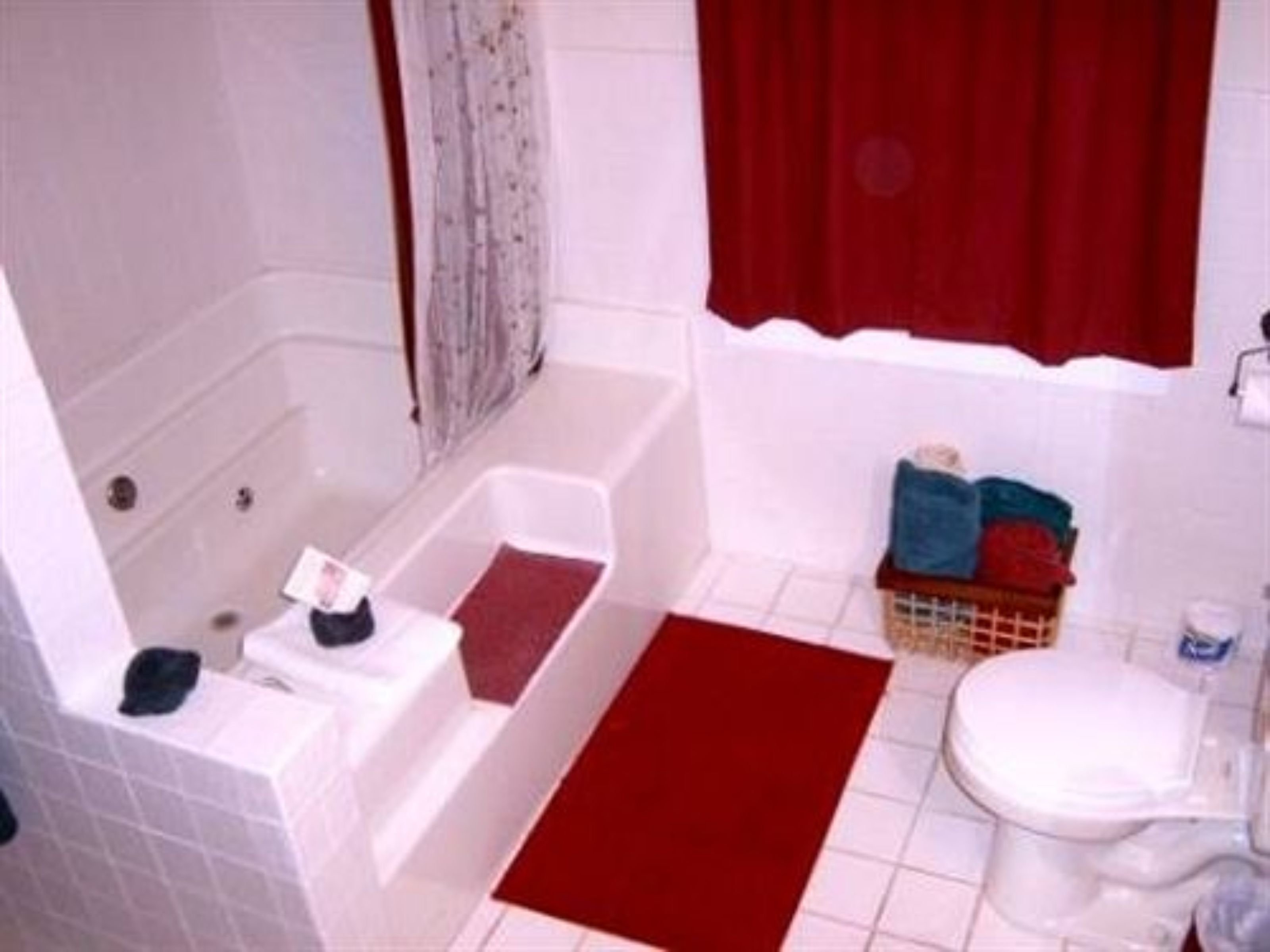 Een badkamer met een bad, toilet en een rode badmat.