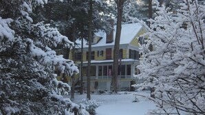 A snow-covered house with a porch and trees in the foreground. - Brookview Manor Inn (Canadensis)