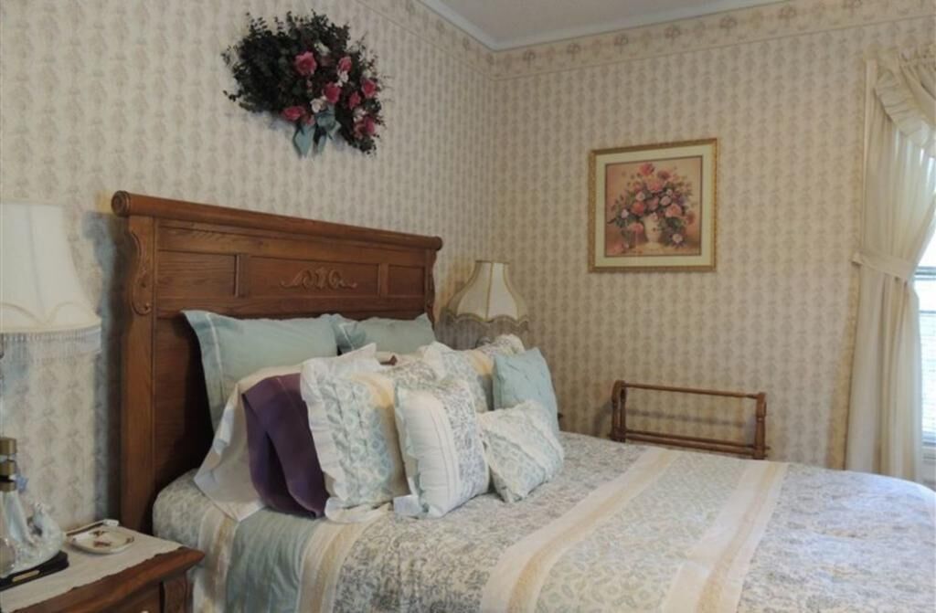 Une chambre à coucher avec une tête de lit en bois, une décoration murale à motifs floraux, un tableau encadré et une table de chevet avec une lampe.