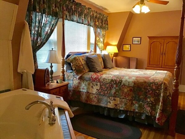 A bedroom with a bed, a nightstand, a lamp, a wooden wardrobe, and a bathroom with a bathtub. - Brookview Manor Inn (Canadensis)
