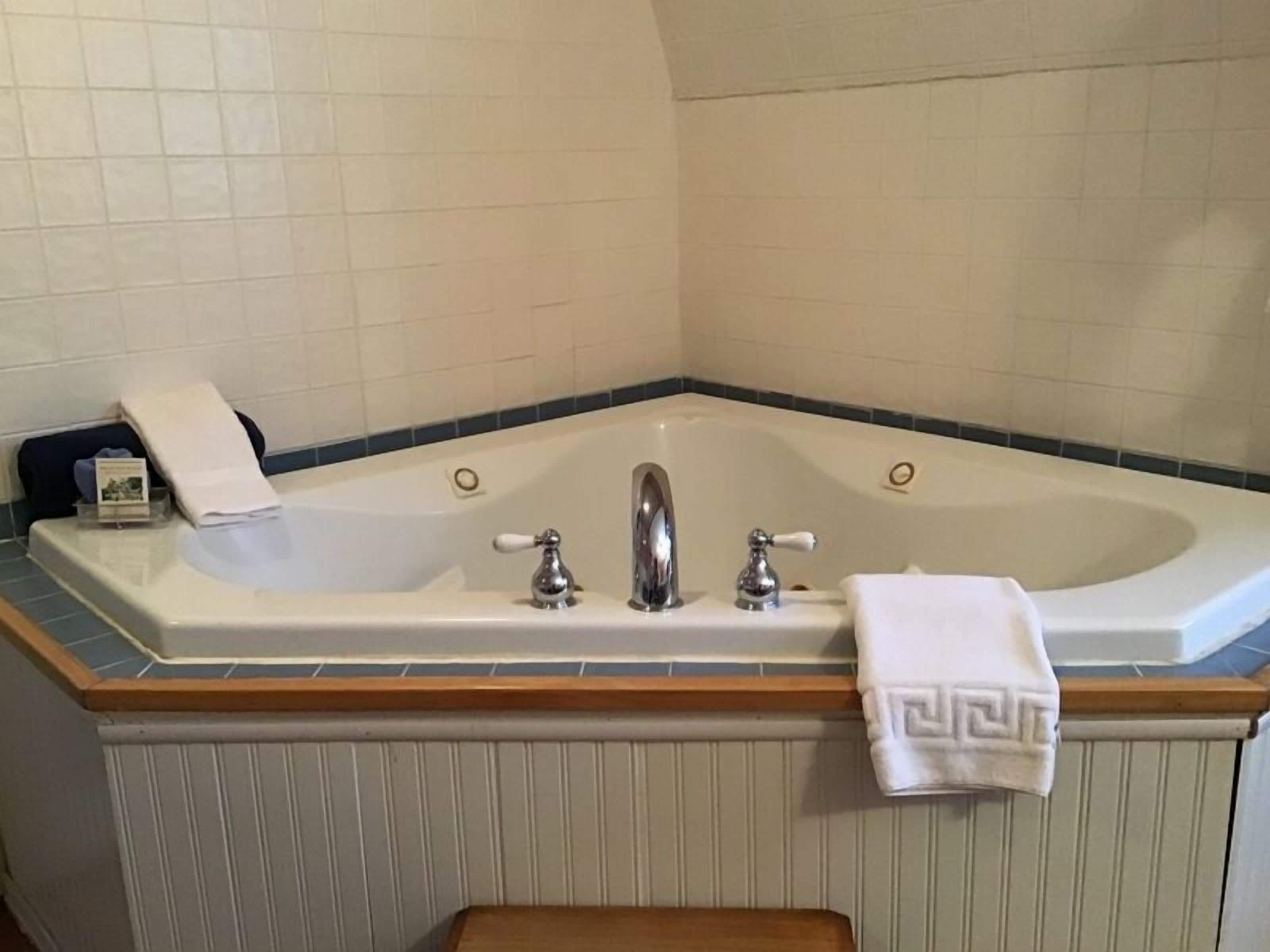 Un baño con una bañera grande, dos llaves y un perchero con toallas.