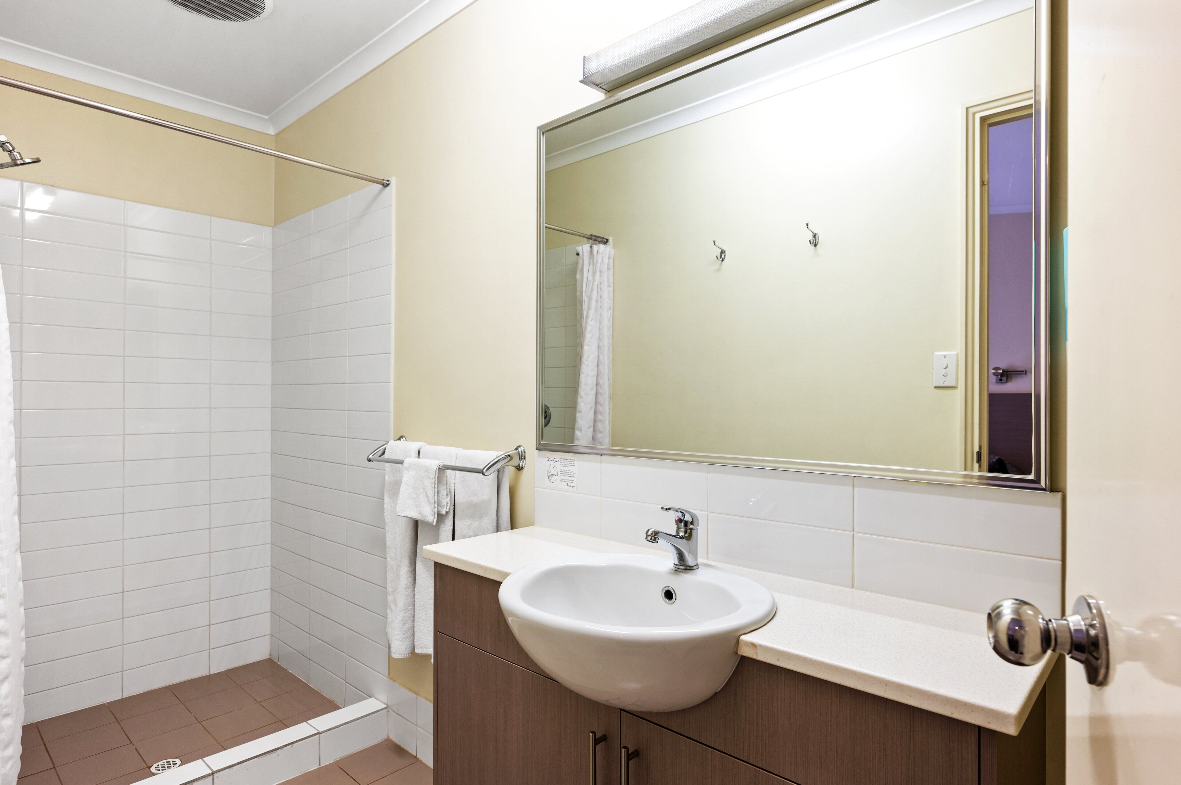 Ein modernes Badezimmer mit einem weißen Waschbecken, beige gestrichenen Wänden und einer Glasdusche.