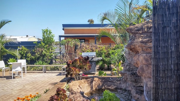Un'area patio con una griglia per barbecue, una piccola cascata e un salotto con sedie.