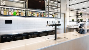 Zona bar moderna con diverse bottiglie di liquori, un grande schermo piatto e un design pulito e minimalista.