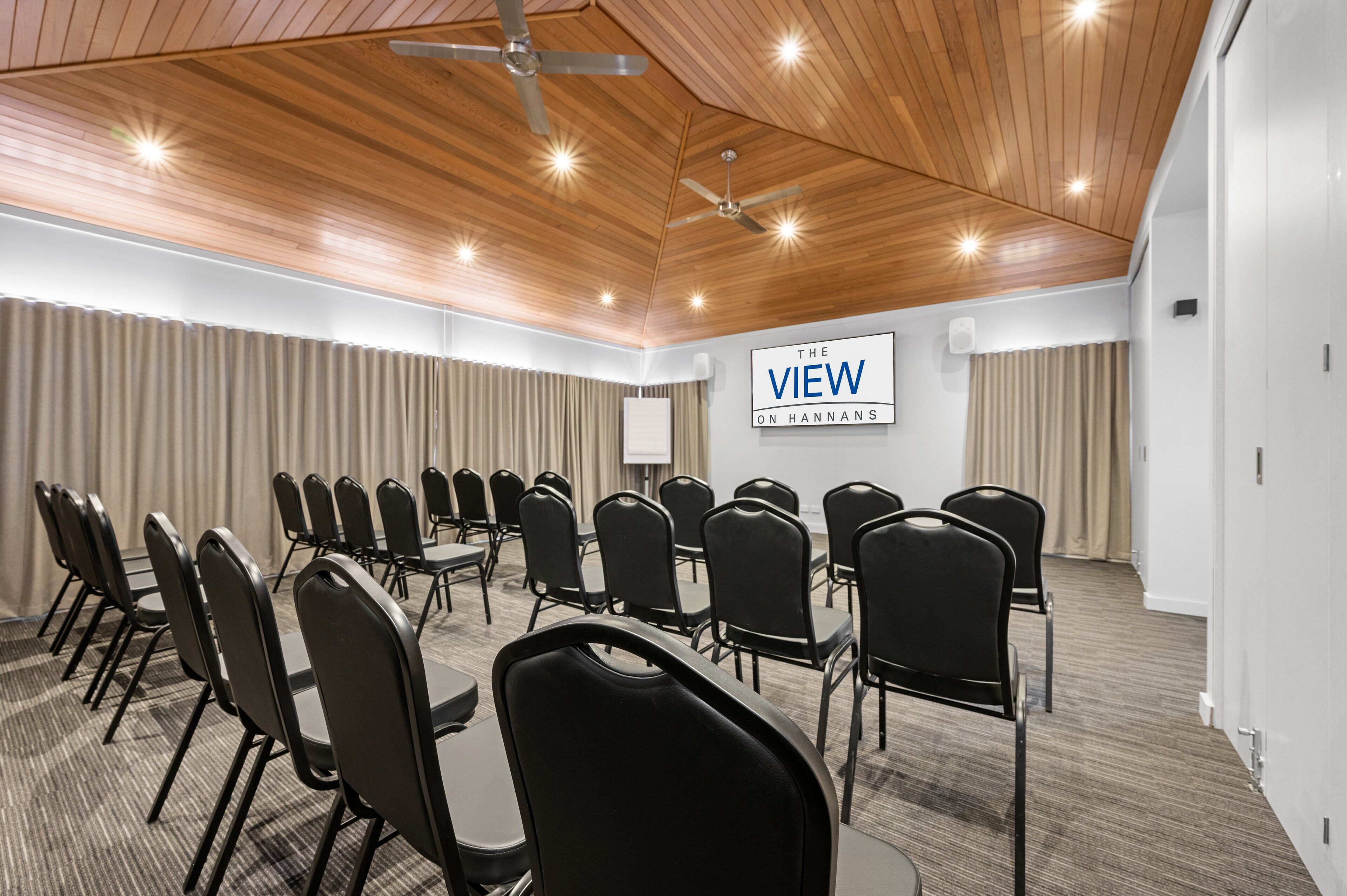 Ein Konferenzraum mit Holzbalkendecke, schwarzen Stühlen, die in U-Form angeordnet sind, einer Whiteboard und einem Schild mit der Aufschrift 'The View on Hannans'.