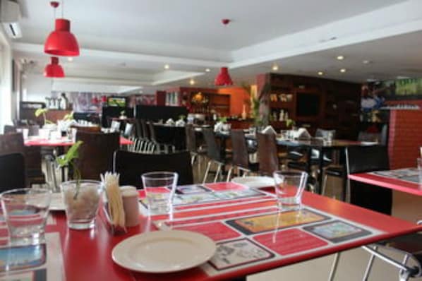 Un interior de restaurante con mesas y sillas rojas, y lámparas colgantes.