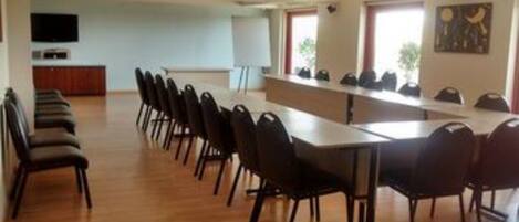 Uma sala de conferência com uma mesa comprida e cadeiras, uma lousa e uma televisão na parede.