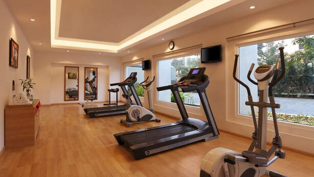 A fitness room with treadmills, an elliptical, and a rowing machine. There are large windows, a clock, and a TV on the wall. - Red Fox by Lemon Tree Hotels, Jaipur (Jaipur)