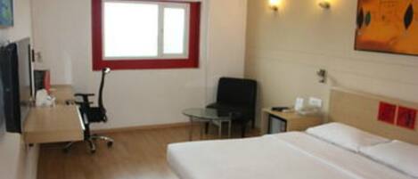 Una habitación de hotel con una cama, un escritorio con una silla, una mesita, un televisor y un ventanal con marco rojo.