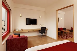 Habitación de hotel con cama, escritorio con silla, televisor y zona de estar con mesa y sillas.