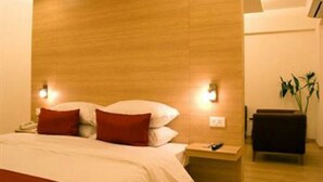 A hotel room with a wooden headboard, a bed with white and red bedding, a bedside table with a lamp, and a small plant. - Red Fox by Lemon Tree Hotels, Jaipur (Jaipur)