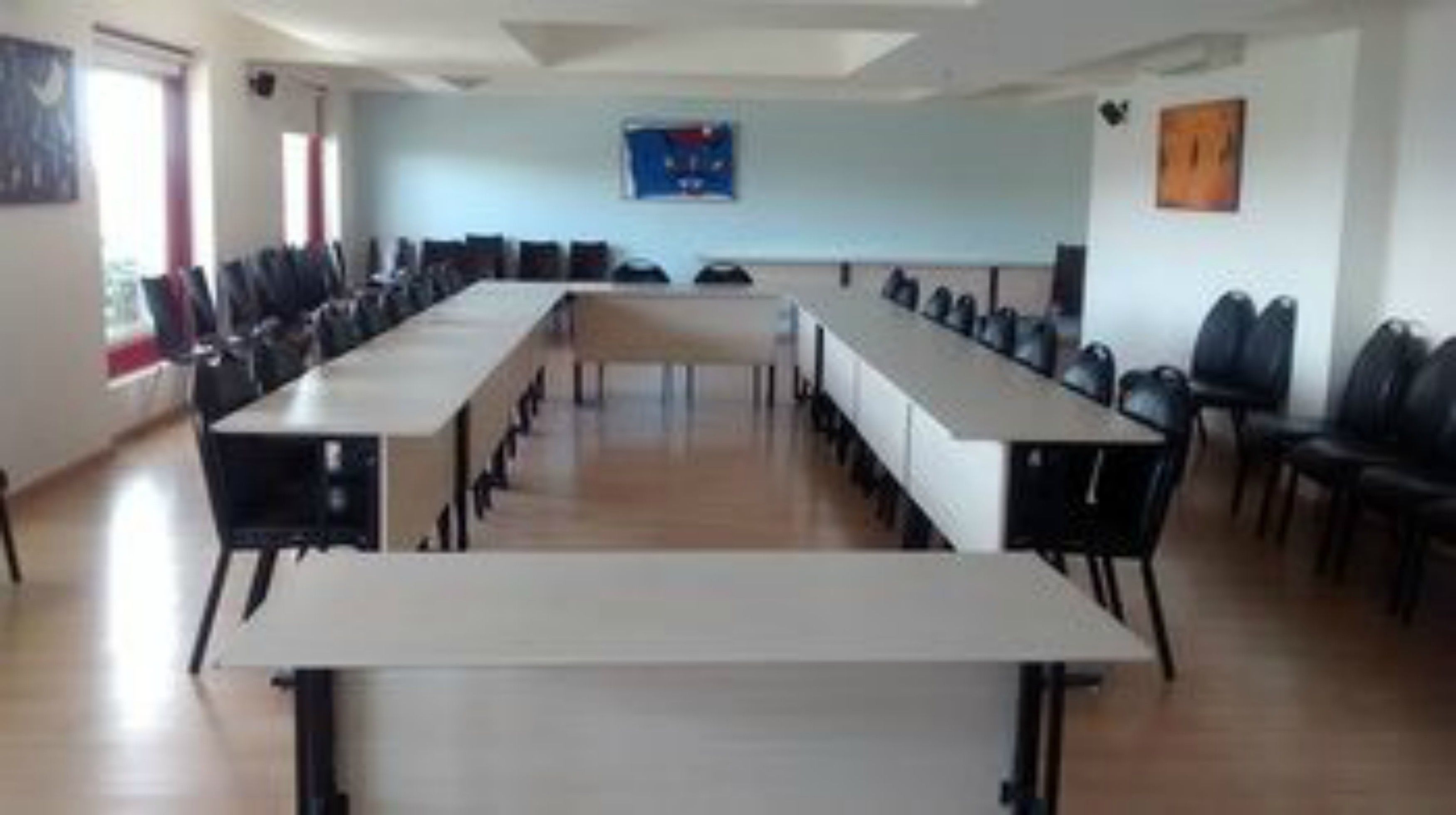 A conference room with long tables and chairs, a large window, and a blue wall with a poster.