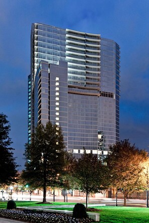 A modern high-rise building with a glass facade, surrounded by trees and a well-maintained lawn. - Loews Atlanta Hotel (Atlanta)