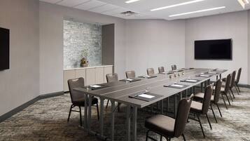 A conference room with a long table, chairs, a flat-screen TV, and a stone accent wall.