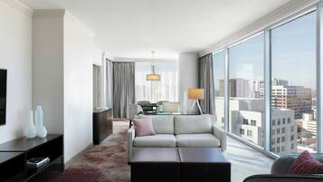 A modern hotel room with a large window, a sofa, a coffee table, a TV, and a lamp.